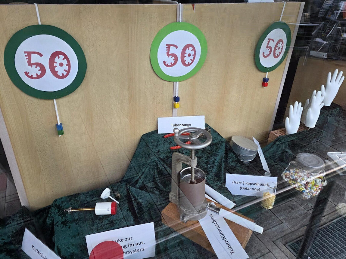 Dekoration im Schaufenster mit drei Symbolbildern 50-Jahre-Hotzenwald-Apotheke und Apotheken-Utensilien